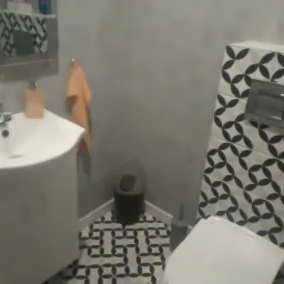 Wykończona łazienka w szaro-białej kolorystyce z wzorzystymi płytkami na podłodze i ścianie, widoczna umywalka z szafką i toaleta.