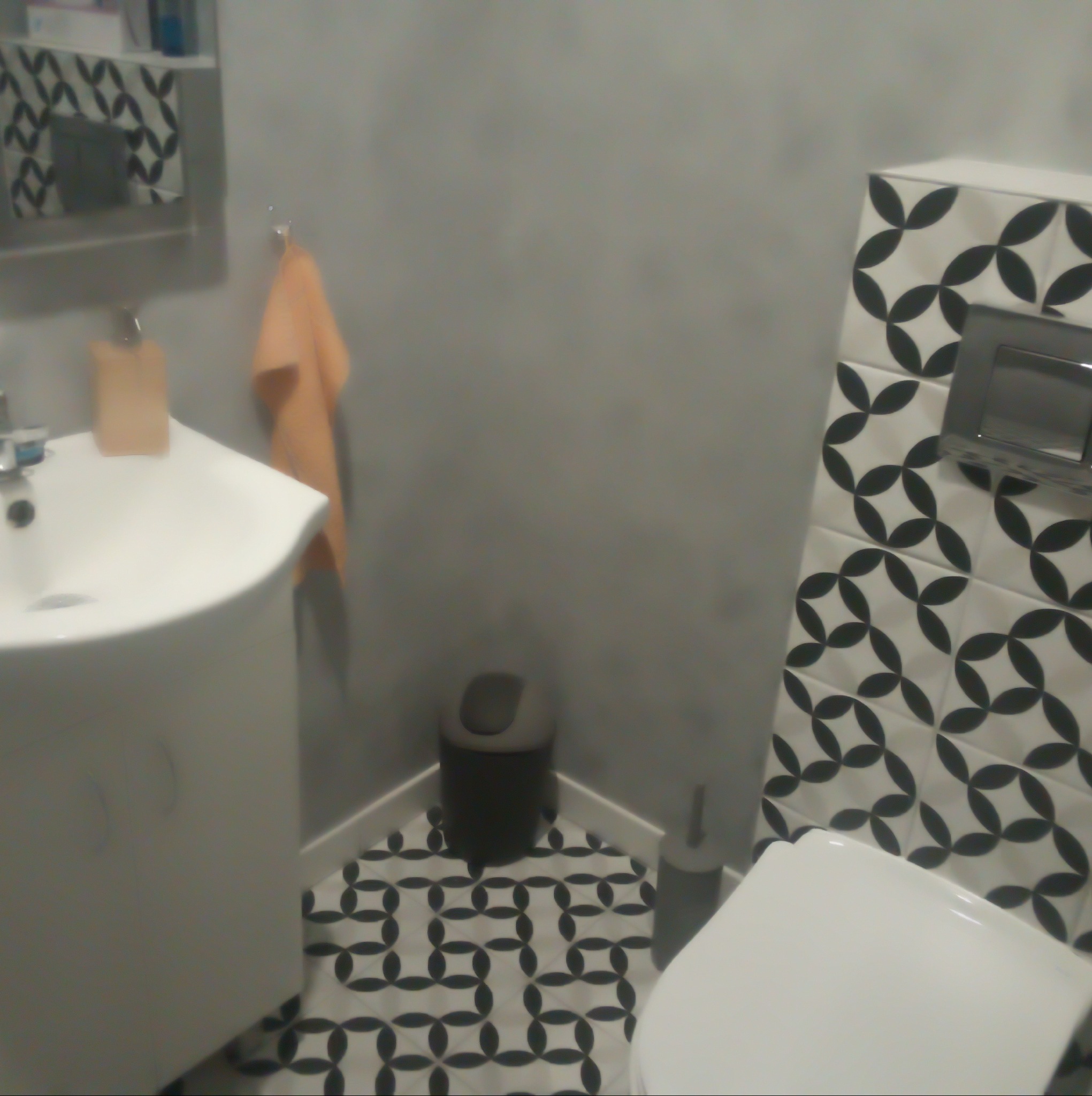 Wykończona łazienka w szaro-białej kolorystyce z wzorzystymi płytkami na podłodze i ścianie, widoczna umywalka z szafką i toaleta.