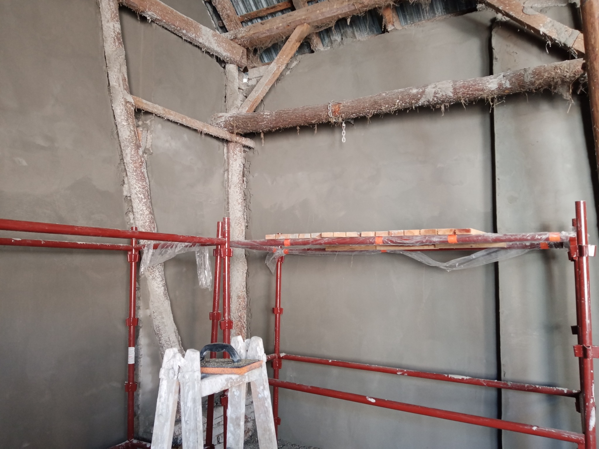 Wnętrze poddasza w trakcie prac tynkarskich, widoczne rusztowanie, drewniana konstrukcja dachu i świeżo otynkowana ściana z widocznymi śladami po tynkowaniu.