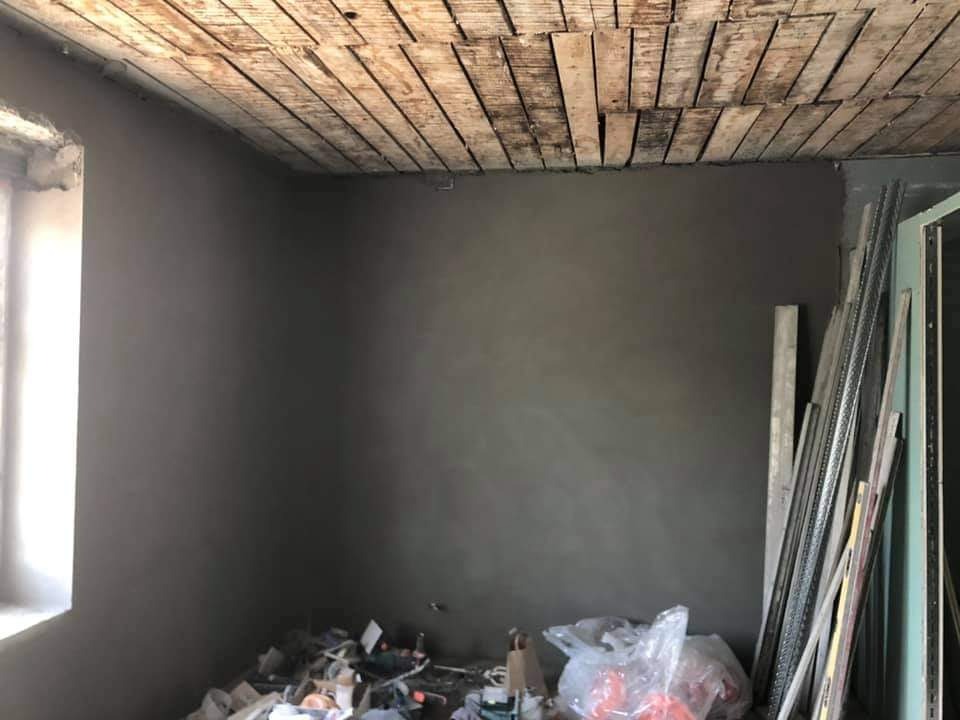 Świeżo otynkowane ściany w pomieszczeniu w Nowym Tomyślu, widoczny surowy drewniany sufit i materiały budowlane przy ścianie.