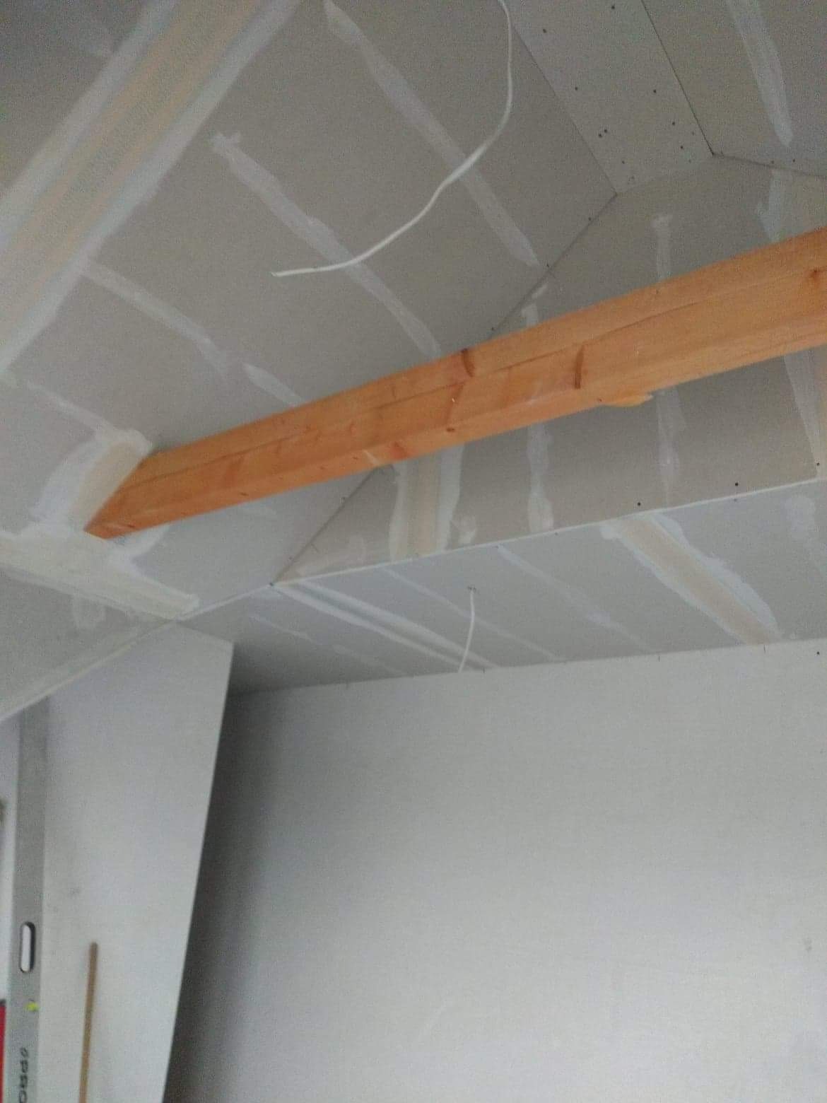 Poddasze w trakcie zabudowy płytami gipsowo-kartonowymi, widoczna drewniana belka konstrukcyjna i szczelina pomiędzy płytami na suficie.