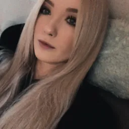 Portret młodej kobiety z długimi, blond włosami, leżącej na miękkiej, futrzanej poduszce, z widoczną kulą świetlną w tle.