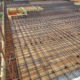 Zbrojenie stropu budynku jednorodzinnego z widocznymi otworami okiennymi w szalunku, przygotowane do zalania betonem, z widocznymi wystającymi prętami pionowymi.