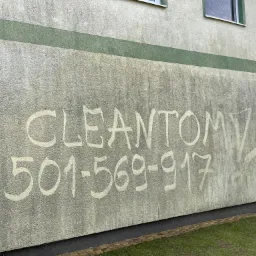 Ściana budynku z szarą elewacją, na której widnieje napis 'CLEANTOM' i numer telefonu 501-569-917, wykonany prawdopodobnie przez brud lub jako reklama przed czyszczeniem. Widoczne okno w górnej...