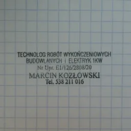 Kadr z bliska na kartkę w kratkę z pieczątką firmy: TECHNOLOG ROBÓT WYKOŃCZENIOWYCH BUDOWLANYCH i ELEKTRYK 1KW, Nr Upr. E1/126/2808/20, Marcin Kozłowski, Tel. 538 211 016.