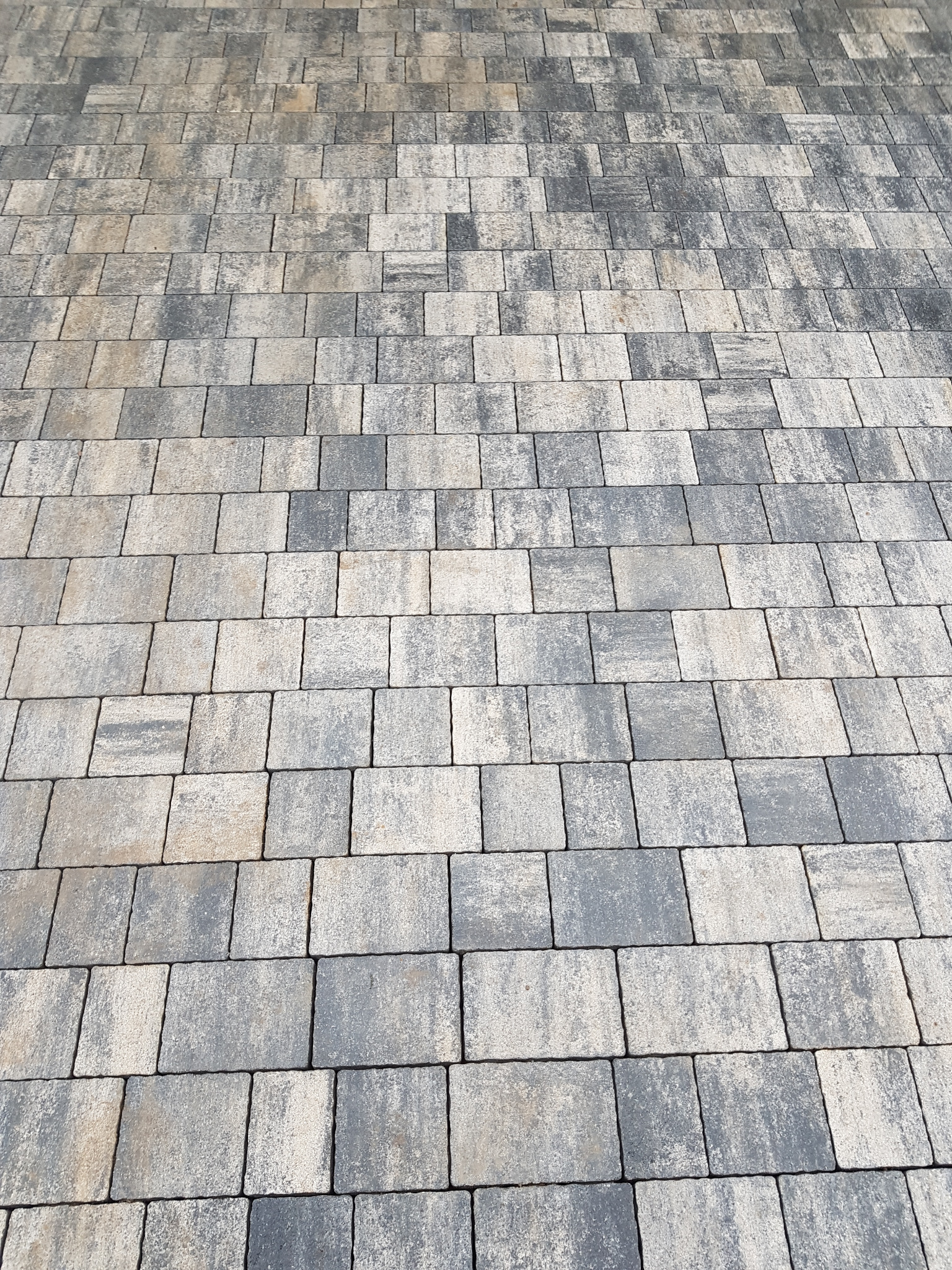 Ułożona kostka brukowa w odcieniach szarości i beżu, widok z perspektywy, z delikatną teksturą i subtelnymi różnicami w kolorze poszczególnych elementów.