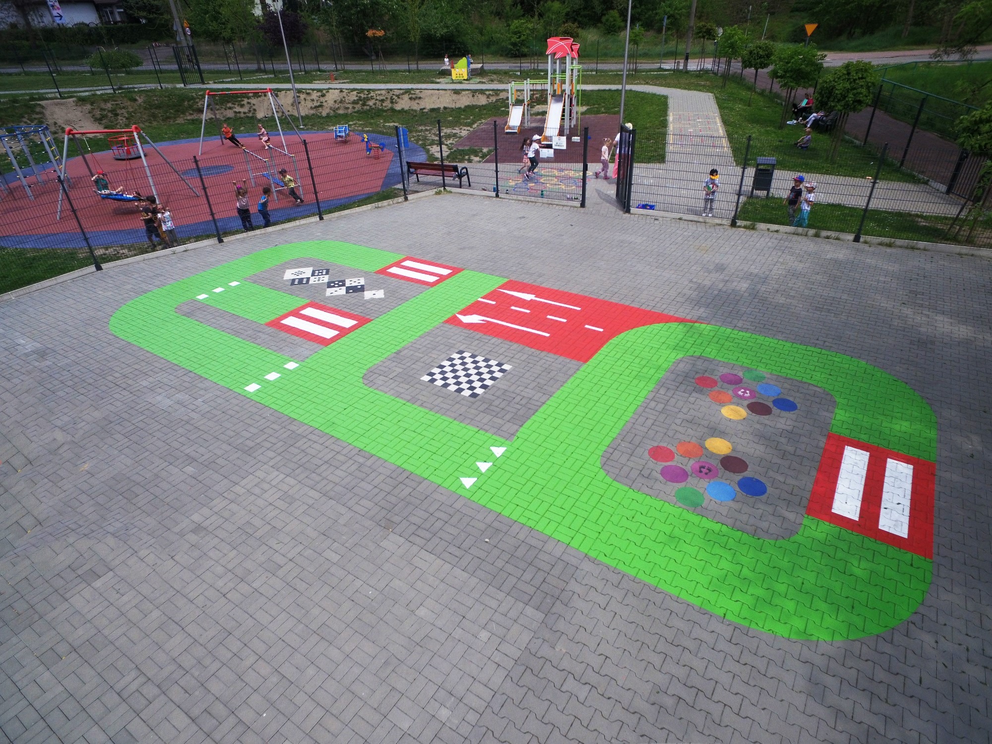 Kolorowa nawierzchnia z motywami drogowymi i edukacyjnymi na terenie placu zabaw w Rybniku, widok z góry, z huśtawkami i zjeżdżalniami w tle.