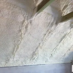 Poddasze po ociepleniu pianką PUR, widoczne drewniane belki i ślady po mocowaniu, jasna, nierówna struktura piany.