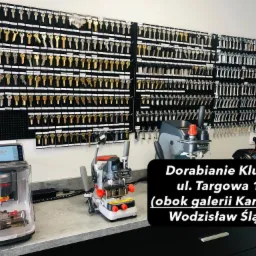 Wnętrze warsztatu: ściana z ekspozycją kluczy różnego typu, obok profesjonalne maszyny do dorabiania kluczy, w tym model Condor z ekranem dotykowym.