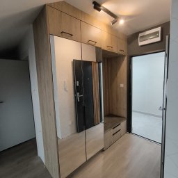 Ir Home Handicrafts Tomaszewski Andrzej - Hall zabudowany szafą z lustrami i siedziskiem w odcieniach drewna, oświetlenie punktowe na suficie, widok na drzwi wejściowe i wewnętrzne.