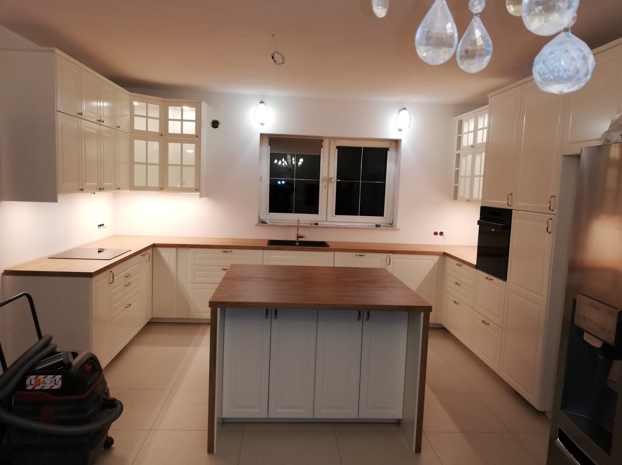 Jasna kuchnia z drewnianymi blatami i wyspą, widoczny odkurzacz przemysłowy, sugerujący niedawny montaż.