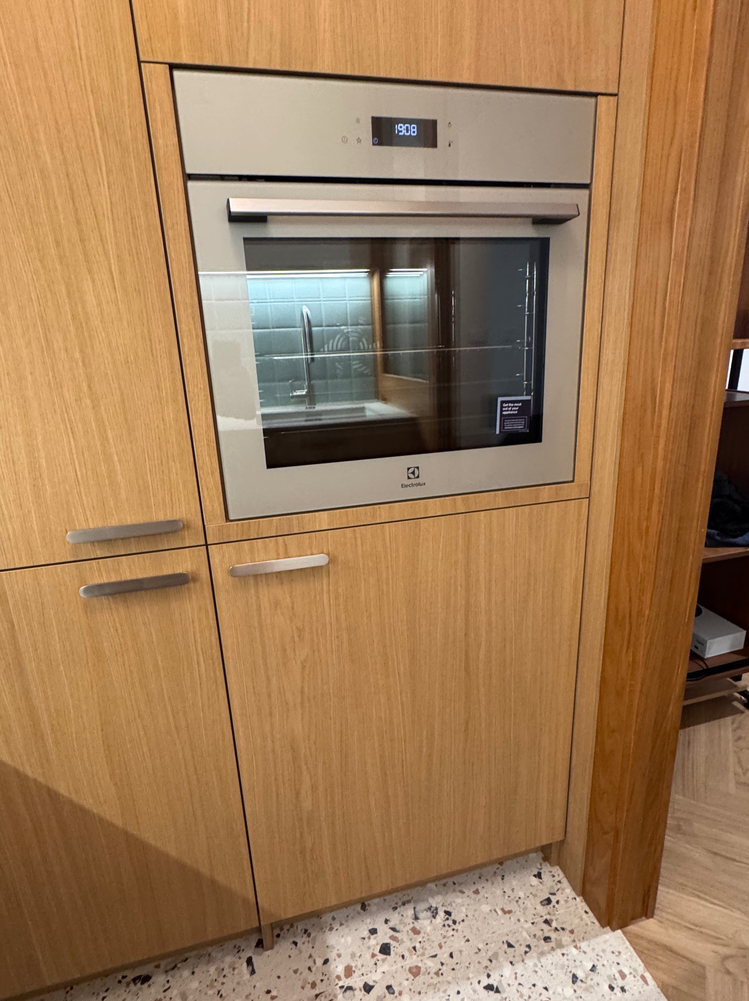 Drewniana zabudowa kuchenna z wbudowanym piekarnikiem Electrolux. Widoczny fragment blatu i podłogi z terazzo. Minimalistyczne uchwyty szafek.