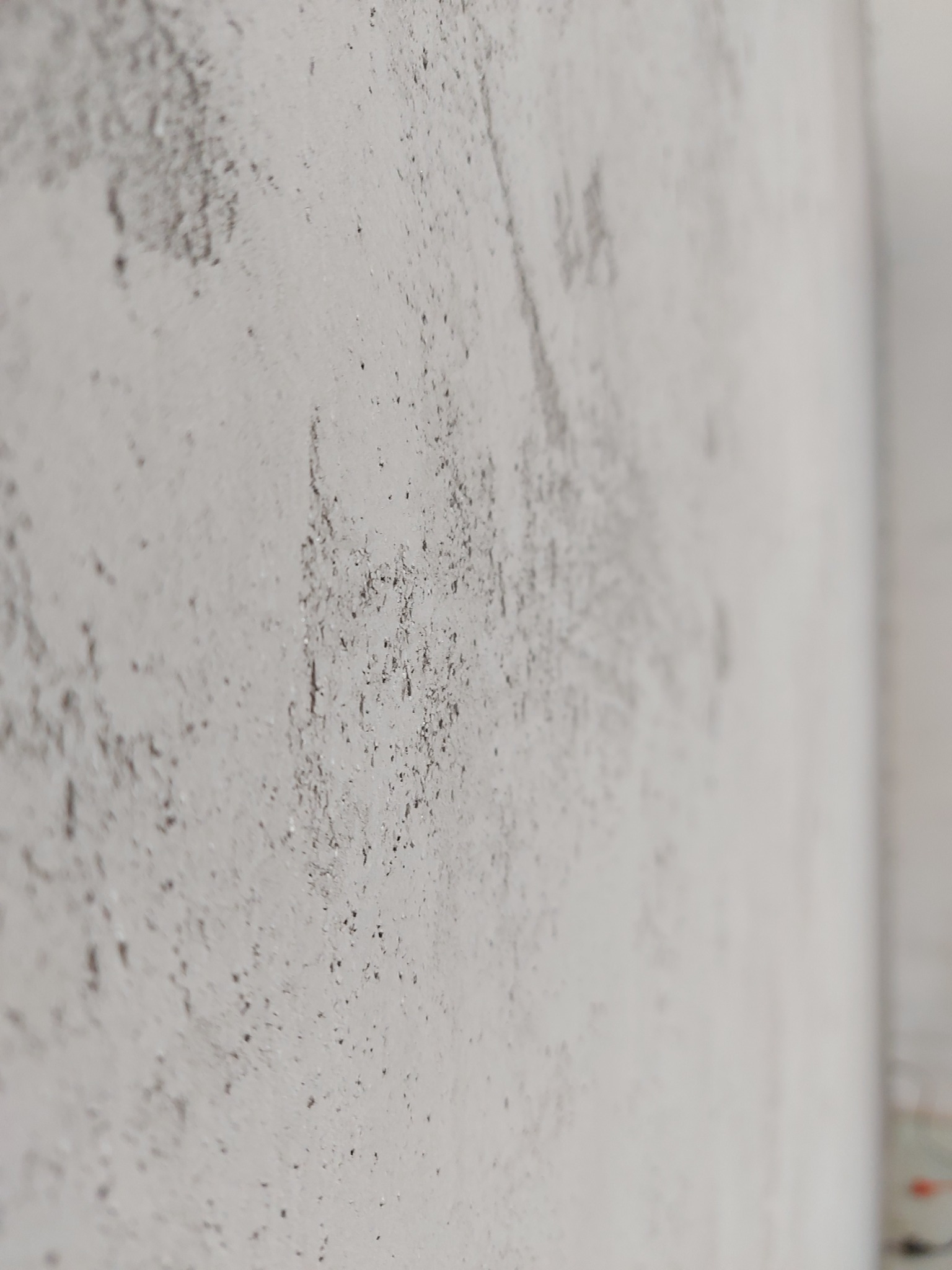 Szpachlowana ściana z widocznymi nierównościami i drobnymi wgłębieniami, przygotowana do dalszych prac wykończeniowych, ujęcie pod kątem.