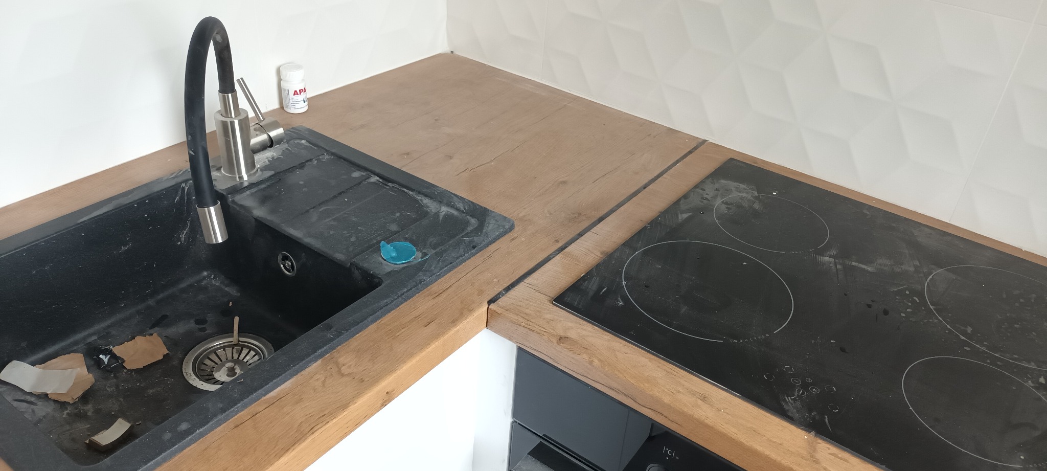Umywalka z czarnego granitu i płyta indukcyjna na drewnianym blacie kuchennym, widoczne ślady po remoncie.