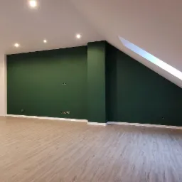 Pomalowane na ciemnozielono ściany w pokoju na poddaszu z oknem dachowym, jasna podłoga imitująca drewno, biały sufit z oświetleniem punktowym i klimatyzacja.