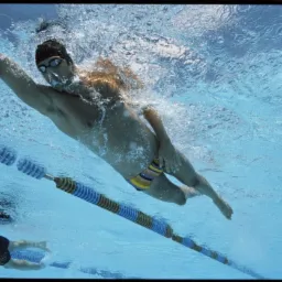 Pływak w czepku i okularach płynie pod wodą stylem dowolnym, widoczny tor pływacki i bąbelki powietrza.