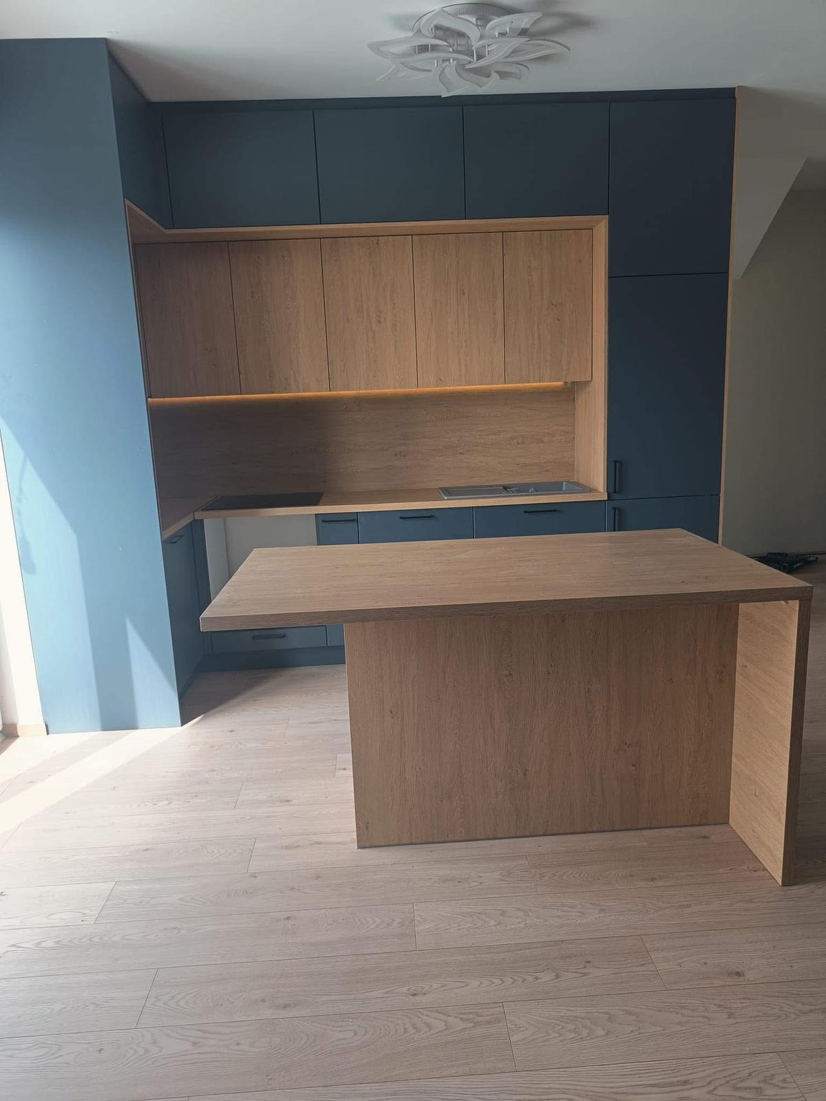 Nowoczesna kuchnia z wyspą: granatowe szafki górne i dolne, drewniane fronty szafek wiszących, oświetlenie LED pod szafkami, drewniana wyspa kuchenna.