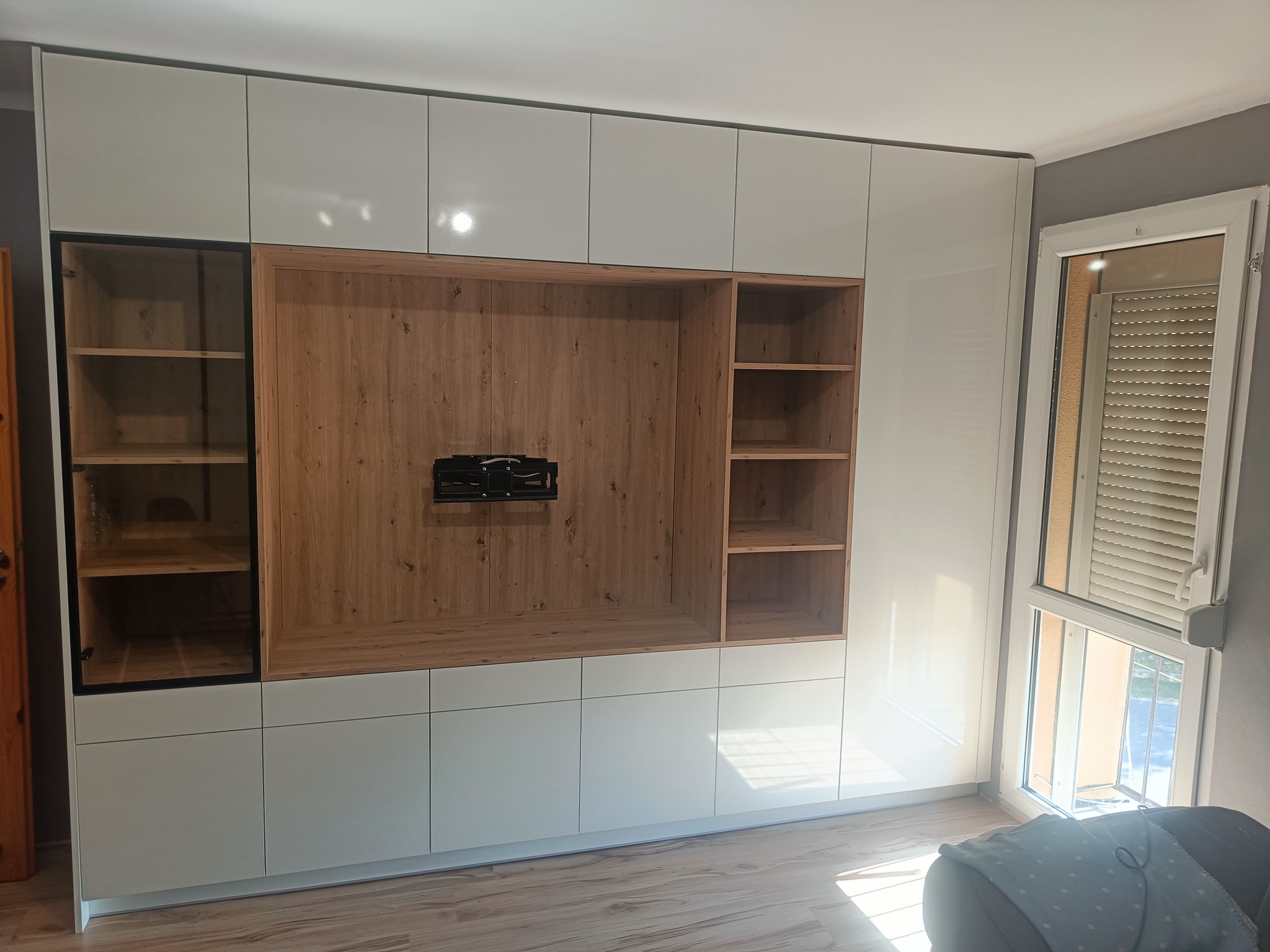 Biała szafa wnękowa z drewnianymi akcentami i miejscem na telewizor, minimalistyczny design, widok z przodu, jasne wnętrze, nowoczesny styl.