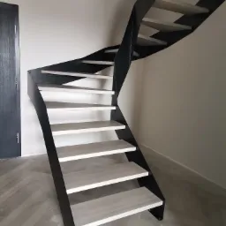 Nowoczesne schody metalowe z drewnianymi stopniami w minimalistycznym wnętrzu, widok z dołu, ciemna rama i jasne stopnie.