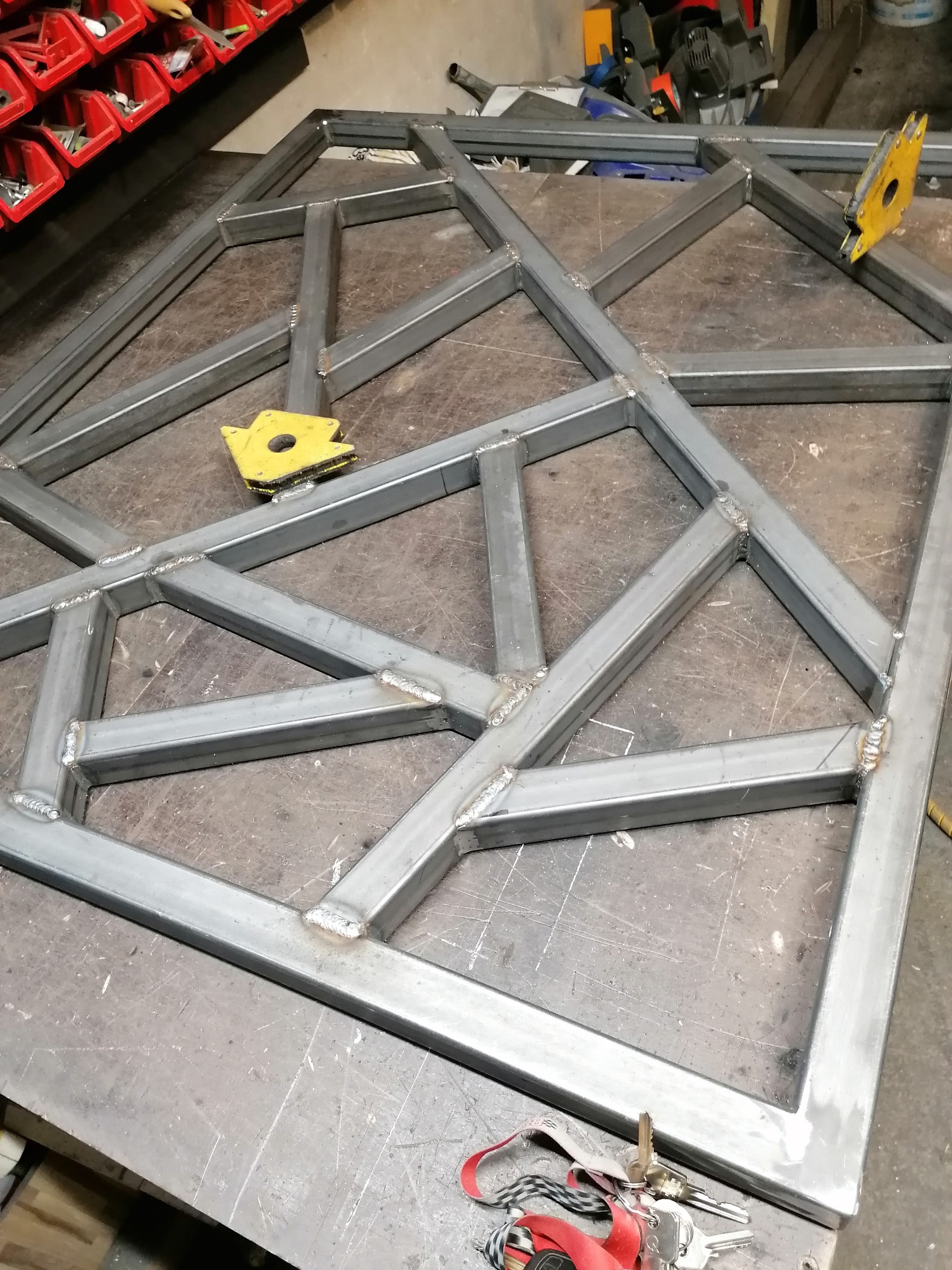 Konstrukcja spawana z metalowych profili o nieregularnym kształcie, leżąca na stole warsztatowym, widoczne spawy i magnesy spawalnicze.