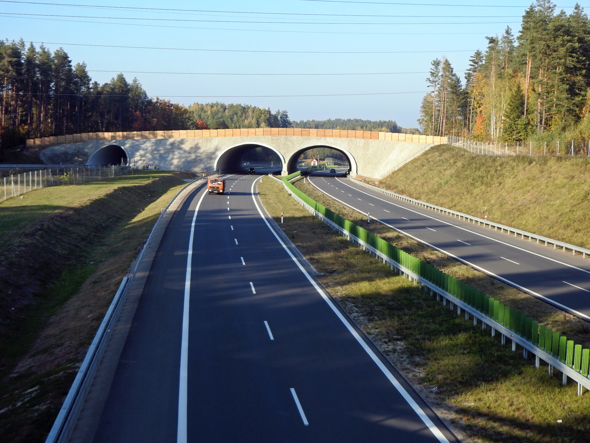 Trasa szybkiego ruchu z trzema pasami w jednym kierunku, nad którą znajduje się betonowy wiadukt z dwoma tunelami dla ruchu drogowego i dodatkowym, mniejszym tunelem po lewej stronie...