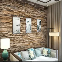 Dekoracyjna ściana z kamienia z trzema obrazami w salonie, oświetlona lampą podłogową i stołową, z sofą z poduszkami w kwiatowe wzory.