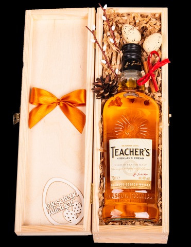 Otwarty drewniany kosz prezentowy z butelką whisky Teacher's, dekoracjami wielkanocnymi: jajkami przepiórczymi, gałązkami bazi i drewnianą ozdobą z napisem 'Wesołego Alleluja!' oraz pomarańczową...
