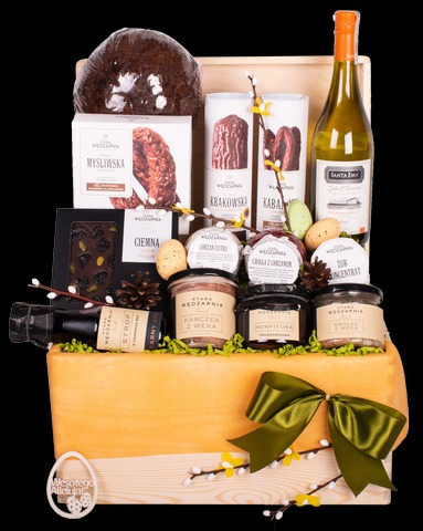 Elegancki kosz upominkowy wypełniony słodyczami i przetworami marki Wedel, butelką wina Santa Ema oraz dekoracjami wielkanocnymi, całość umieszczona w drewnianej skrzynce z zieloną kokardą.