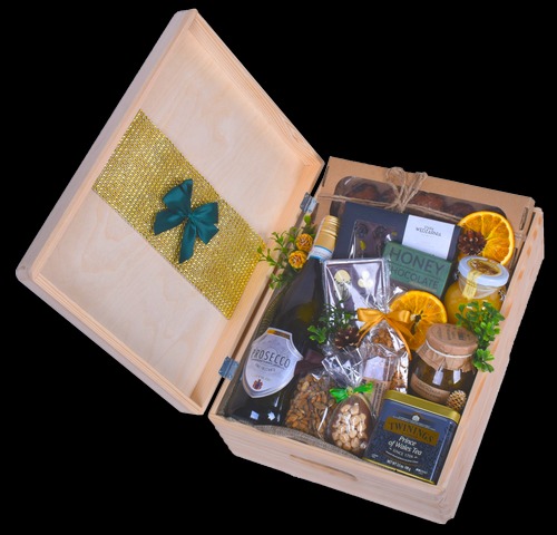 Otwarty drewniany kosz prezentowy z Prosecco, miodem, czekoladą, orzechami, herbatą Twinings i suszonymi pomarańczami, ozdobiony złotą wstążką z zieloną kokardą.