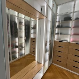Unikkon Hanna Makowska - Nowoczesna garderoba z podświetlanymi półkami i szufladami z jasnego drewna, widok z perspektywy wejścia, parkiet w jodełkę na podłodze.