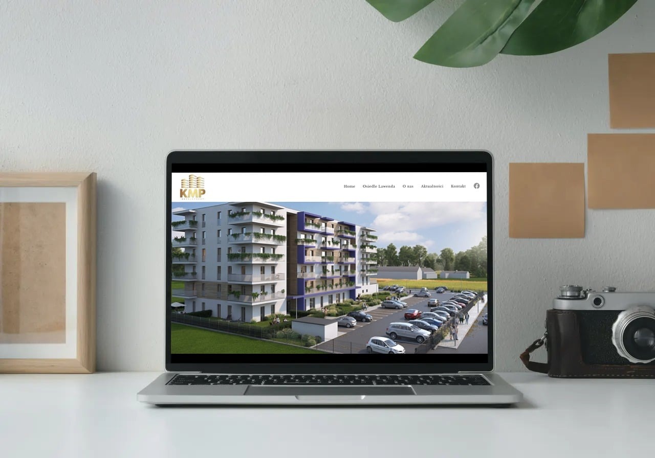 Laptop wyświetla stronę internetową z wizualizacją nowoczesnego budynku mieszkalnego z parkingiem, obok ramka na zdjęcia i aparat retro.
