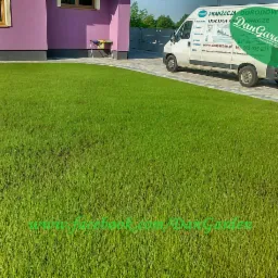 Zadbany trawnik przed fioletowym domem, z kostką brukową i zaparkowanym busem firmy ogrodniczej DanGarden. Widoczny adres strony internetowej.