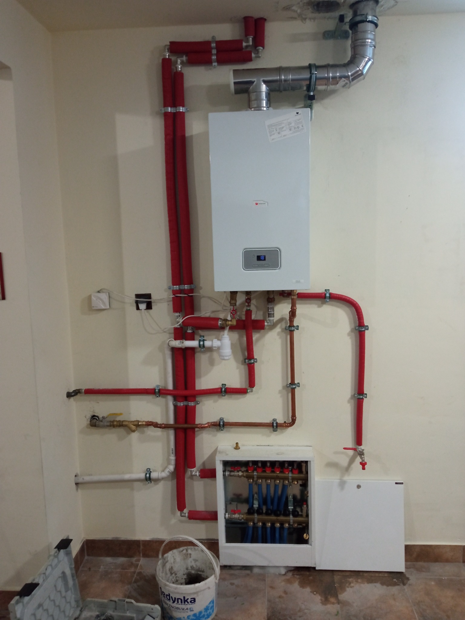 Nowoczesny piec gazowy z podłączeniem instalacji CO w Owieczkach, widoczne rury w izolacji, rozdzielacz ogrzewania podłogowego i przewody kominowe.
