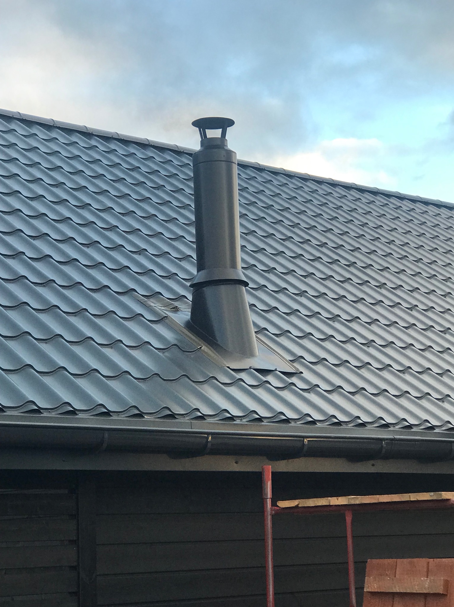 Metalowy komin na dachu z blachy w Połczynie-Zdroju. Widoczny fragment drabiny i rynny. Komin odprowadza dym, co sugeruje jego użytkowanie.