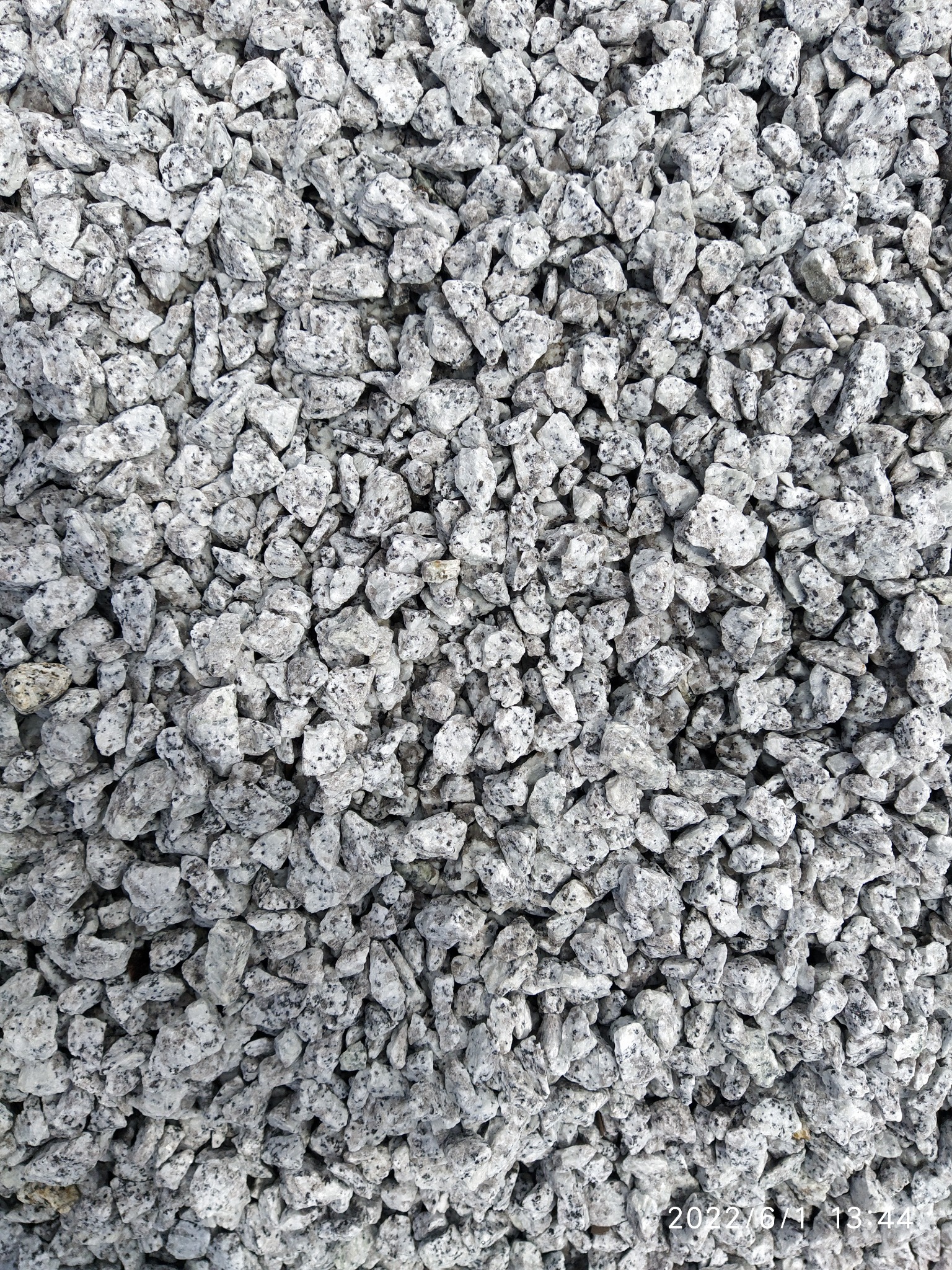 Góra drobnego, białego kruszywa granitowego z czarnymi plamkami, ułożonego gęsto obok siebie.