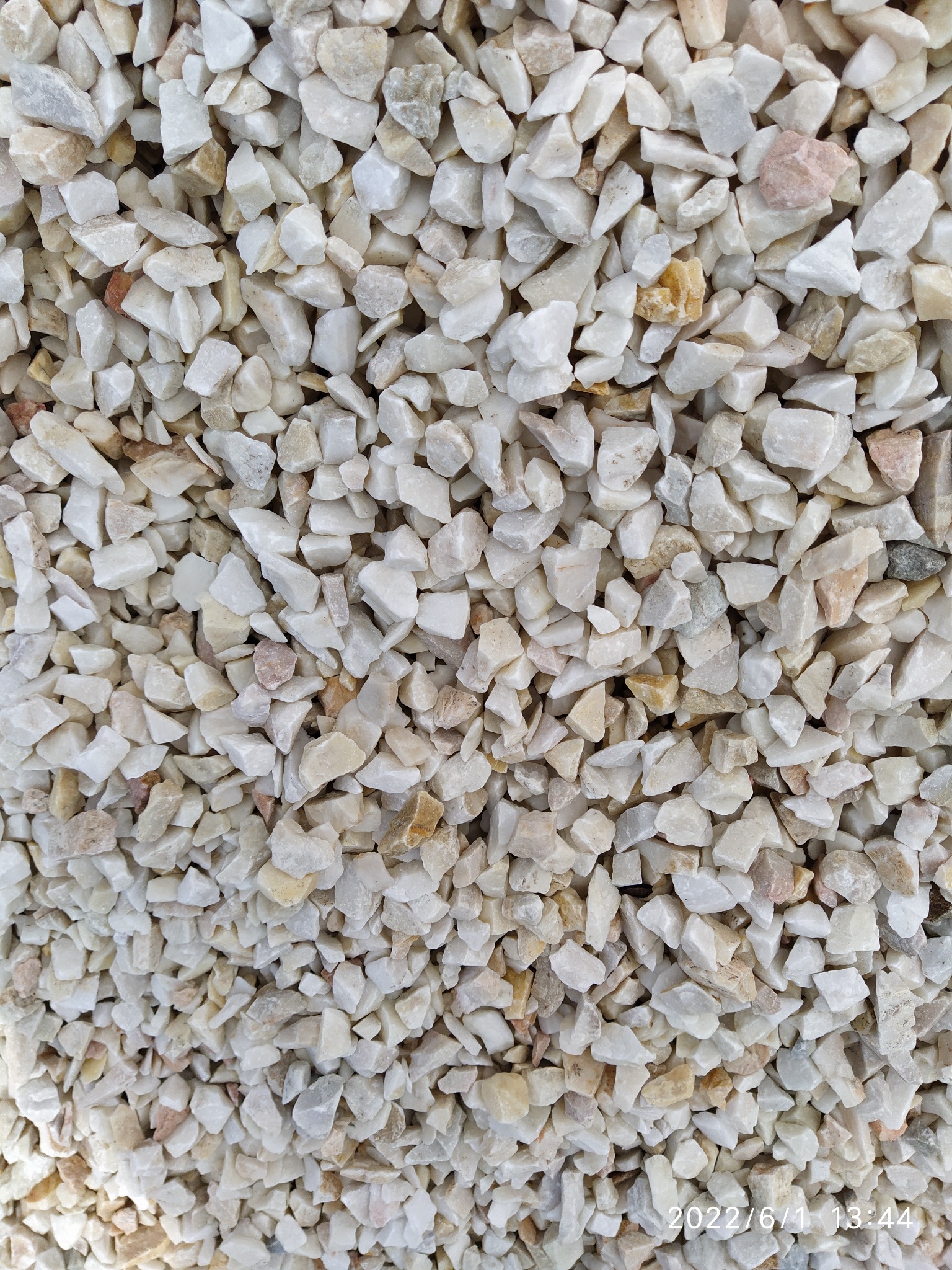 Białe i beżowe drobne kamienie ozdobne, różnej wielkości i kształtu, tworzące jednolitą powierzchnię. Widoczne delikatne różnice w odcieniach i fakturze poszczególnych kamyczków.