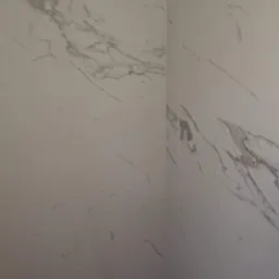 Ściana wyłożona białymi płytkami imitującymi marmur, widoczny narożnik z fugą.