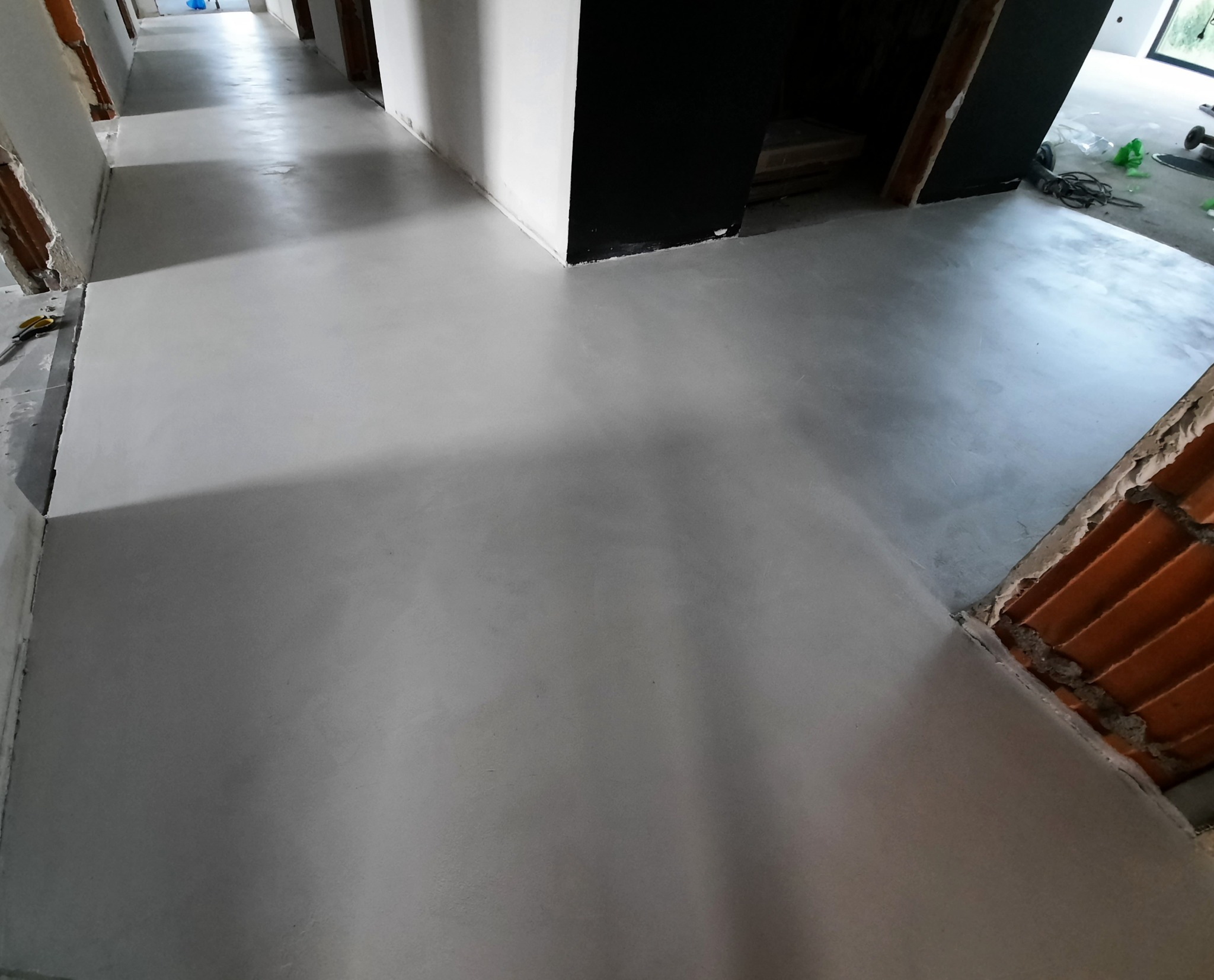 Świeżo wylana, szara posadzka w korytarzu domu we Wrocławiu, widoczne surowe ściany i fragmenty instalacji przed wykończeniem.