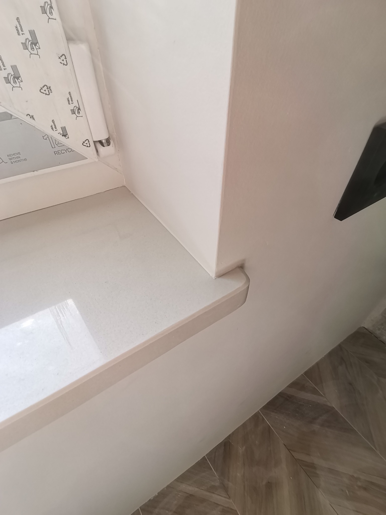 Wykończony parapet wewnętrzny z białego konglomeratu, widoczne fragmenty białej ściany i podłogi wyłożonej płytkami imitującymi drewno.