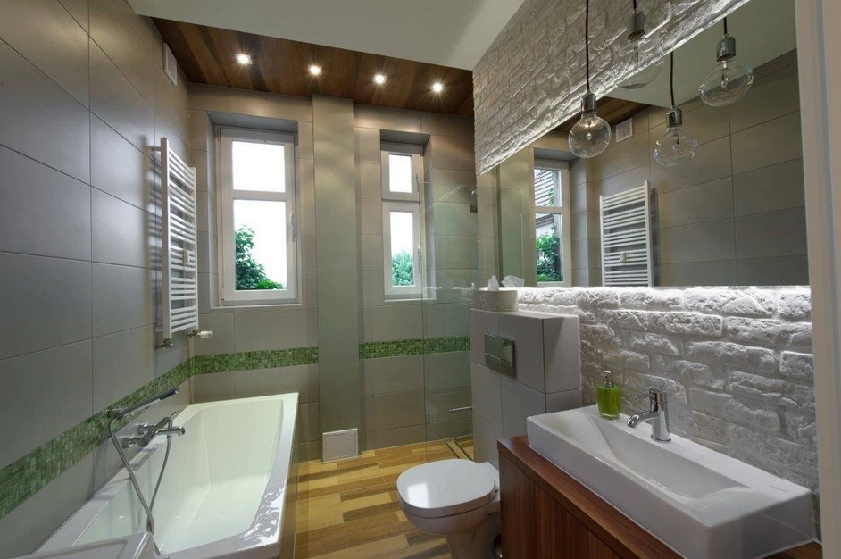 Nowoczesna łazienka z szarymi płytkami, drewnianym sufitem i akcentem białej cegły, oświetlona wiszącymi żarówkami Edison