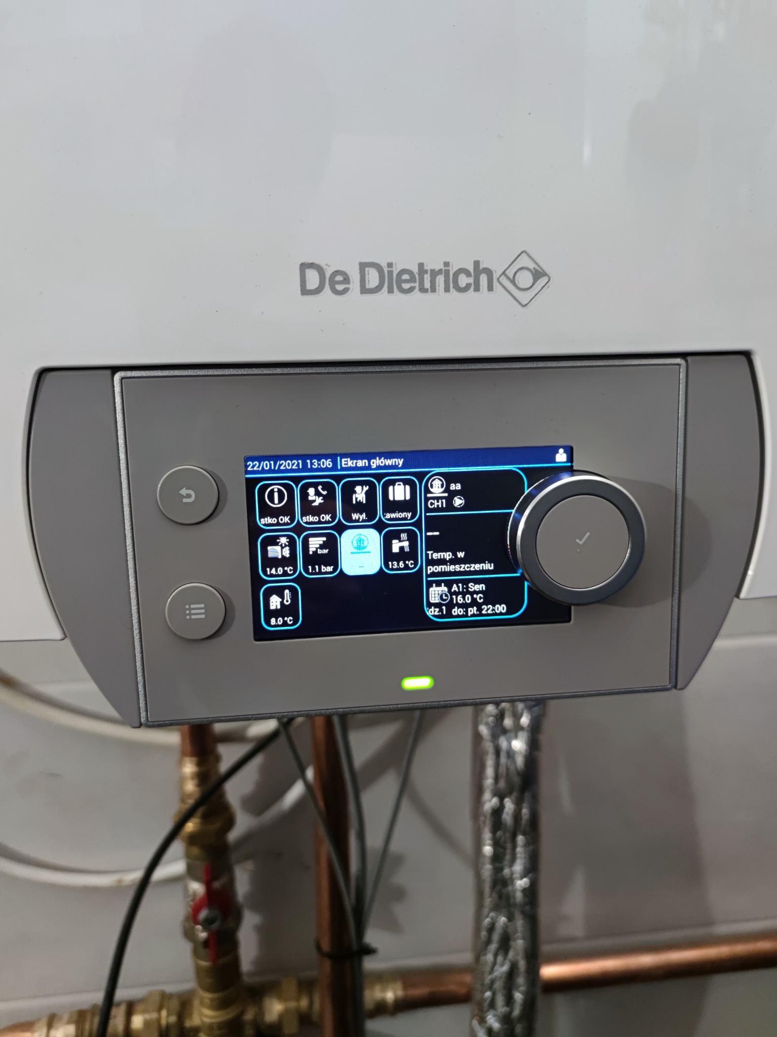 Panel sterowania kotła grzewczego De Dietrich z wyświetlaczem pokazującym temperaturę i ustawienia, widoczne miedziane rury instalacji grzewczej.