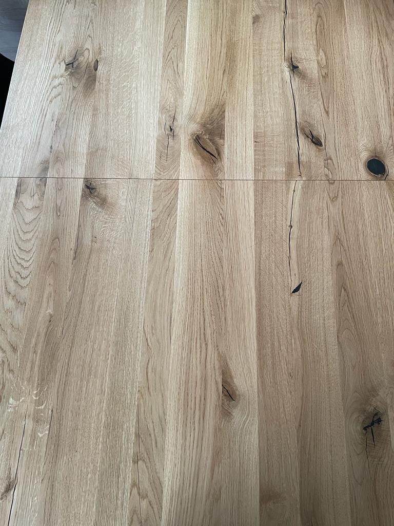 Blat drewniany z wyraźnym usłojeniem, połączony z dwóch części, widoczne naturalne sęki i pęknięcia, jasne drewno.