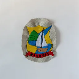 Naszywka z herbem miejscowości Małdyty, przedstawiającym żaglówkę na wodzie, drzewo i wstęgę z nazwą, na szarym tle