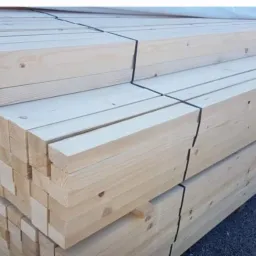 Stos belek z jasnego drewna, spiętych czarną taśmą, widoczne sęki i naturalny rysunek drewna.