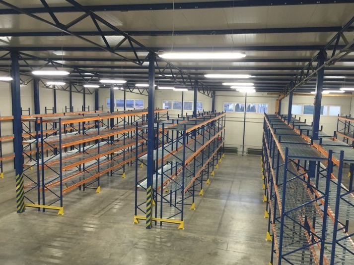 Puste, metalowe regały magazynowe w przestronnym, jasnym magazynie z betonową posadzką, widok z góry.