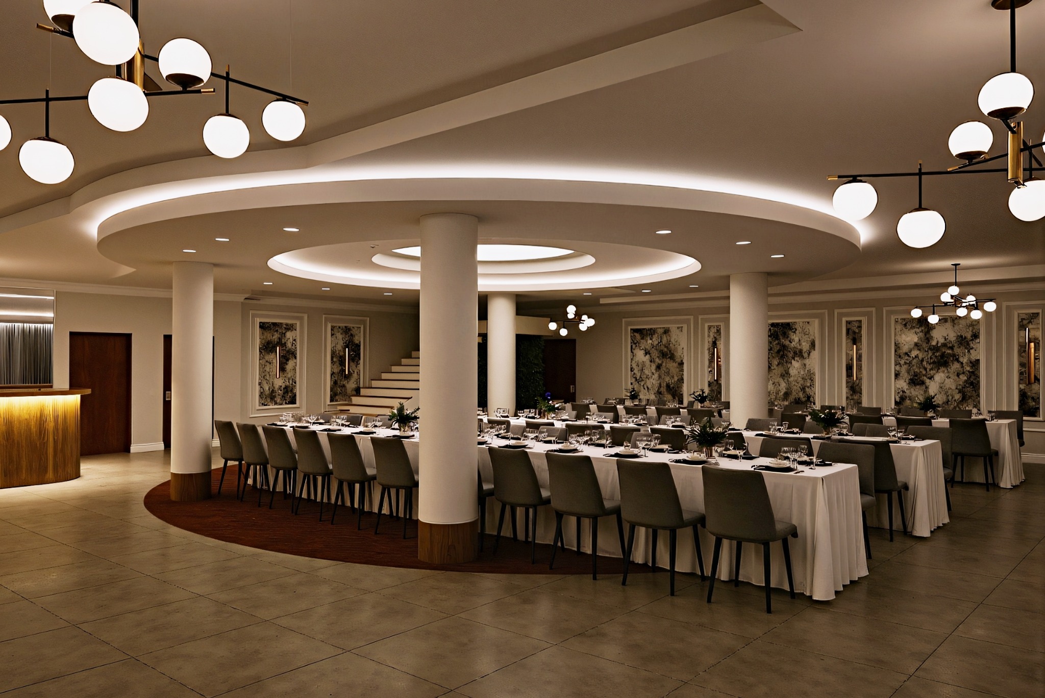 Elegancka sala bankietowa z długimi stołami nakrytymi białymi obrusami, szarymi krzesłami i nowoczesnym oświetleniem. Dekoracyjne panele ścienne i kolumny dodają szyku.