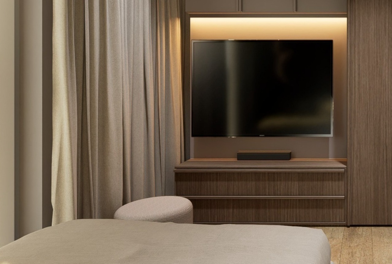 Nowoczesna sypialnia z telewizorem w zabudowie, zasłony w odcieniach beżu, minimalistyczny puf i łóżko. Ciepłe oświetlenie LED podkreśla detale.