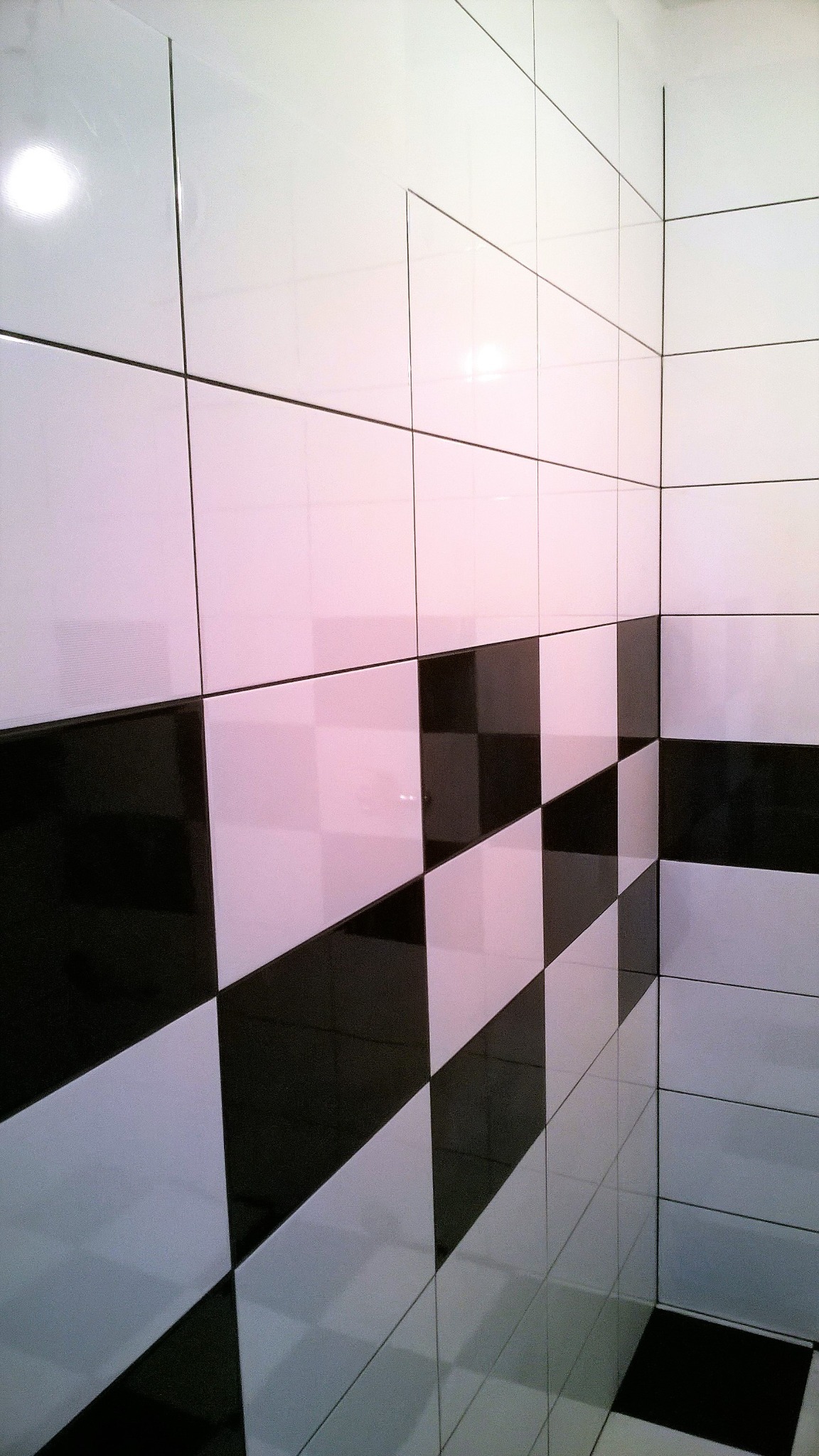 Ściana i podłoga wyłożone błyszczącymi, kwadratowymi płytkami w szachownicę z czarnych i białych płytek, widok z niskiego kąta w rogu pomieszczenia.