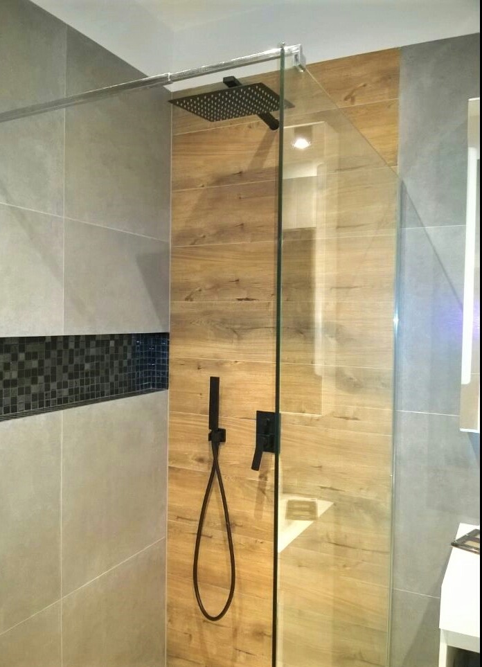 Nowoczesna kabina prysznicowa z czarną armaturą, drewnopodobnymi płytkami na ścianie i szarymi płytkami z mozaiką, widok na deszczownicę i baterię.