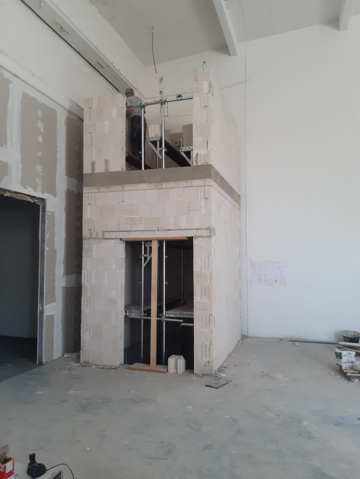 Wnętrze w Kcyni w trakcie prac budowlanych: wznoszenie konstrukcji z bloczków, widoczne rusztowanie i płyty karton gips na ścianie.